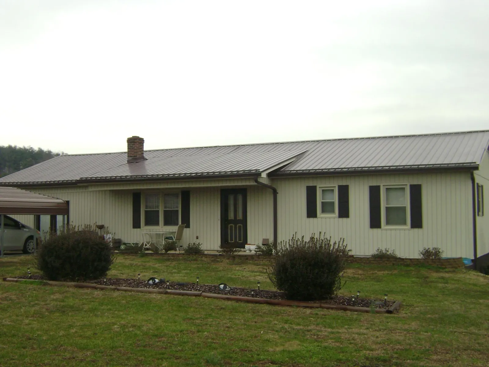 Brown metal roof on a cream sided ranch home with a brick chimney in Milford